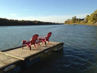 Deux chaises rouges Adirondack posées sur un quai en bois flottant sur une rivière paisible.
