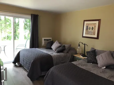 Intérieur d’une chambre de motel comprenant deux lits et une grande porte-fenêtre.