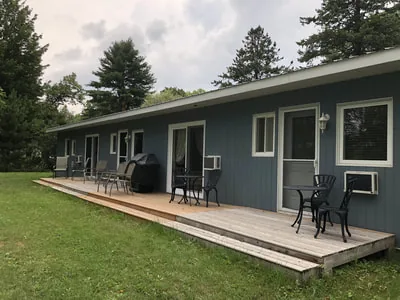 Une terrasse en bois longe un bâtiment bleu équipé de chaises et de tables.